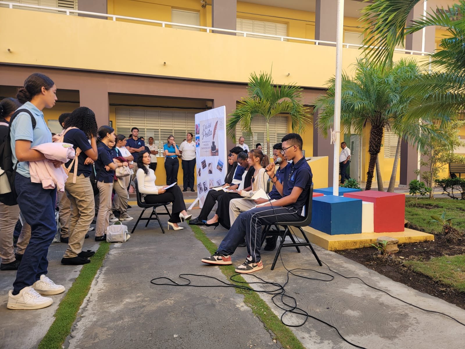 Panel Los poetas durante el acto en el patio del centro, con la maestra de ceremonias al lado