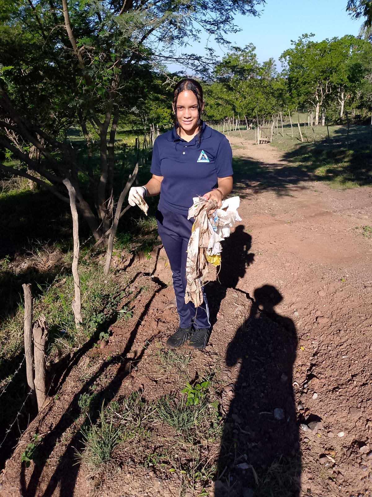Estudiante con guantes sostiene los residuos que recogió junto al camino