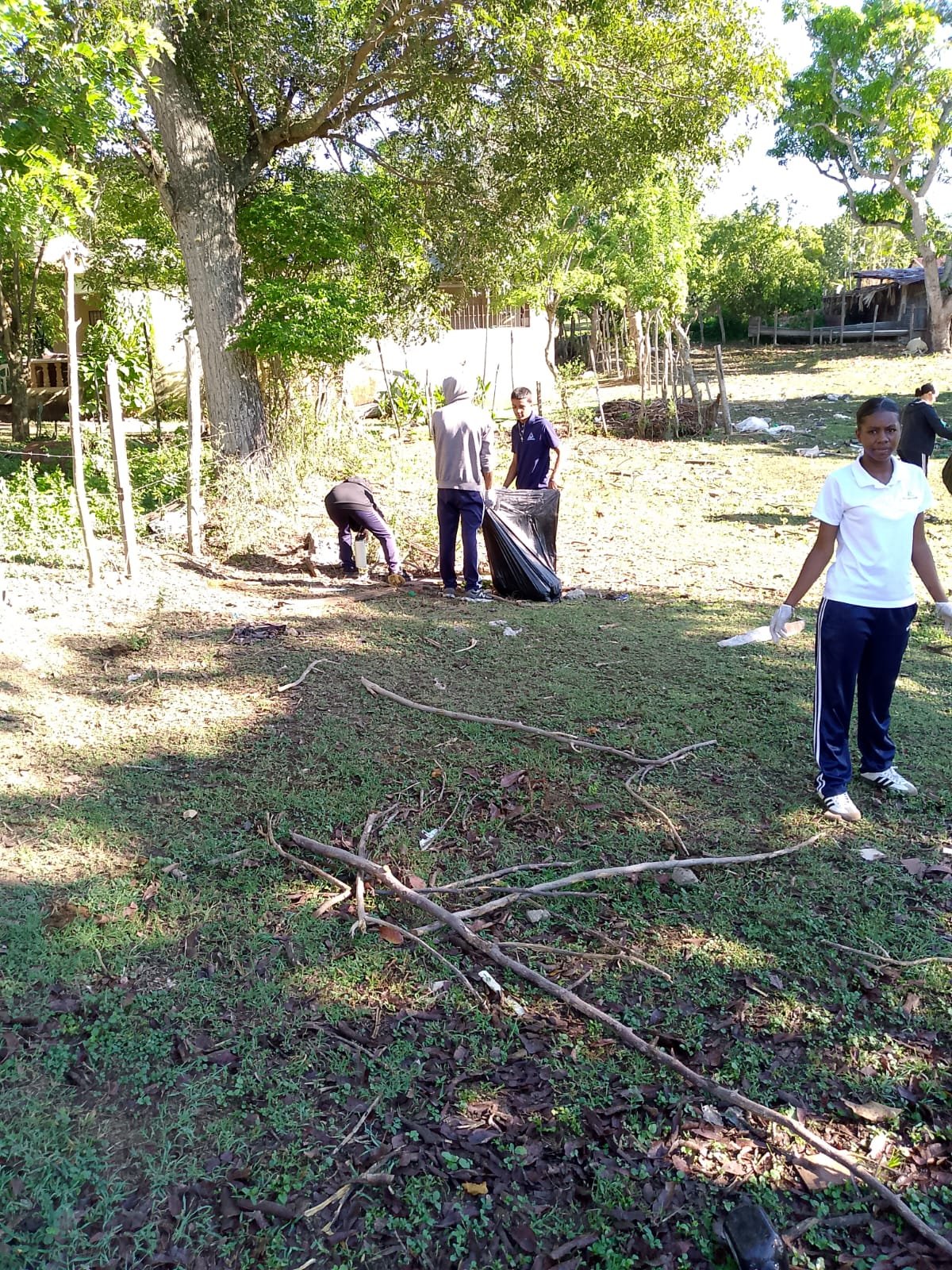 Estudiantes recogen ramas y basura en un patio de la comunidad