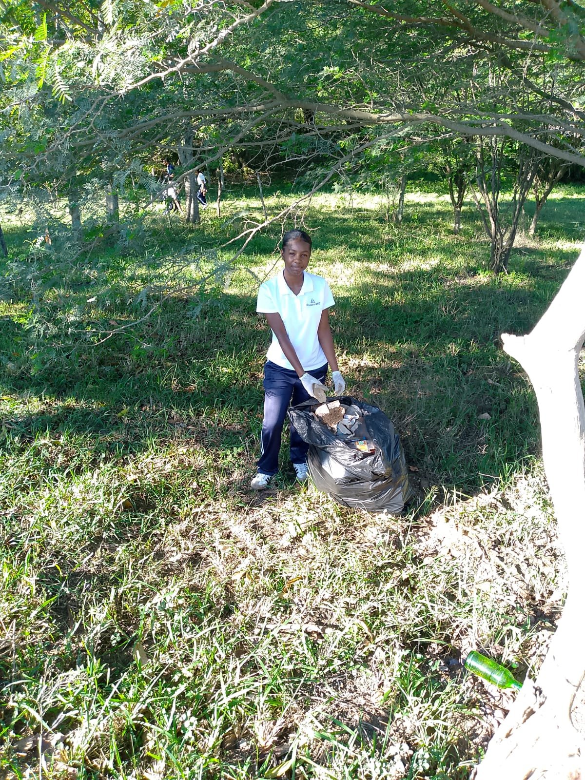 Estudiante con una bolsa de basura recogiendo residuos bajo los árboles